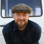 Jared Melrose Campbell, co-founder of Van Life Diaries, in a flat cap leaning on the back of his camper van
